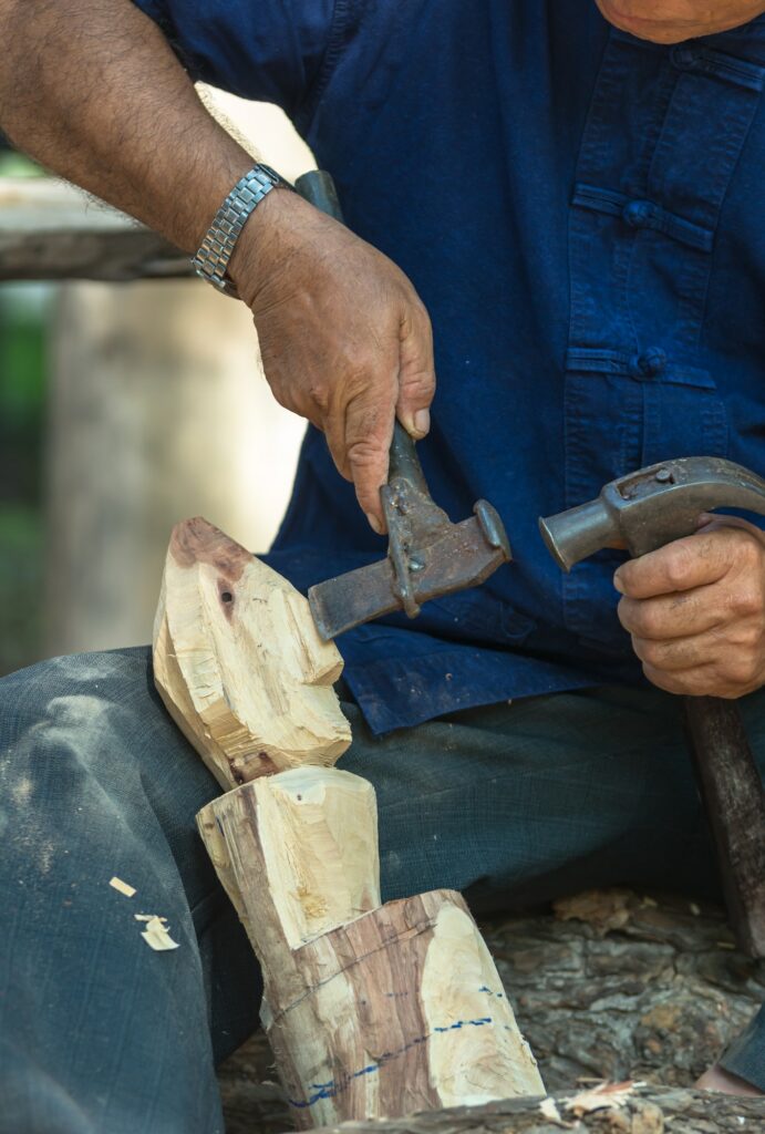 Closeup hand holding hammer and cleaver is making Buddha statue from wood, traditional handcraft
